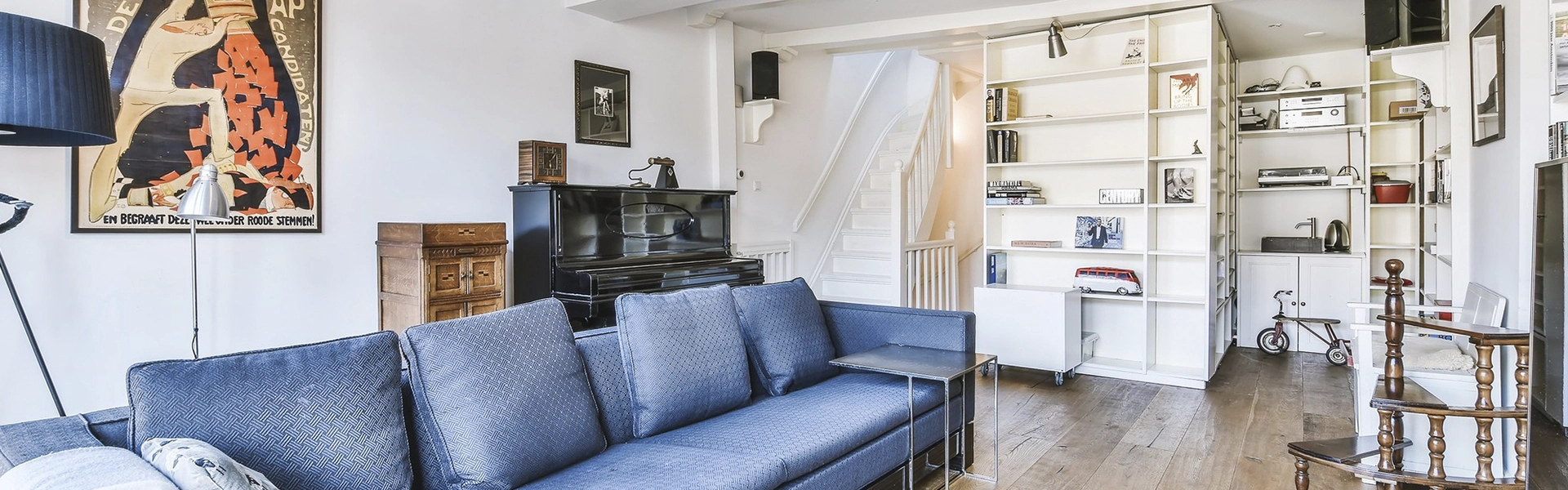 Salón de una casa con un sofá azul, suelo de madera y estanterías y paredes blancas